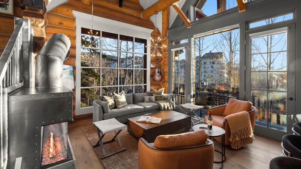 L’intérieur d’une cabane en rondins, avec une cheminée, de grandes fenêtres, un canapé et une table basse.