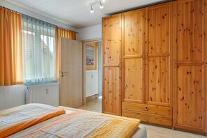 A bedroom with a bed, wooden wardrobe, and a window with curtains.