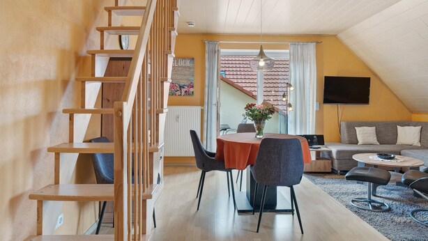 Een modern interieur met een houten trap, een eethoek met een ronde tafel en stoelen, een bank en een televisie.