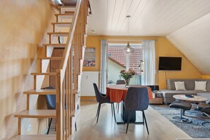 A modern interior with a wooden staircase, a dining area with a round table and chairs, a sofa, and a TV.