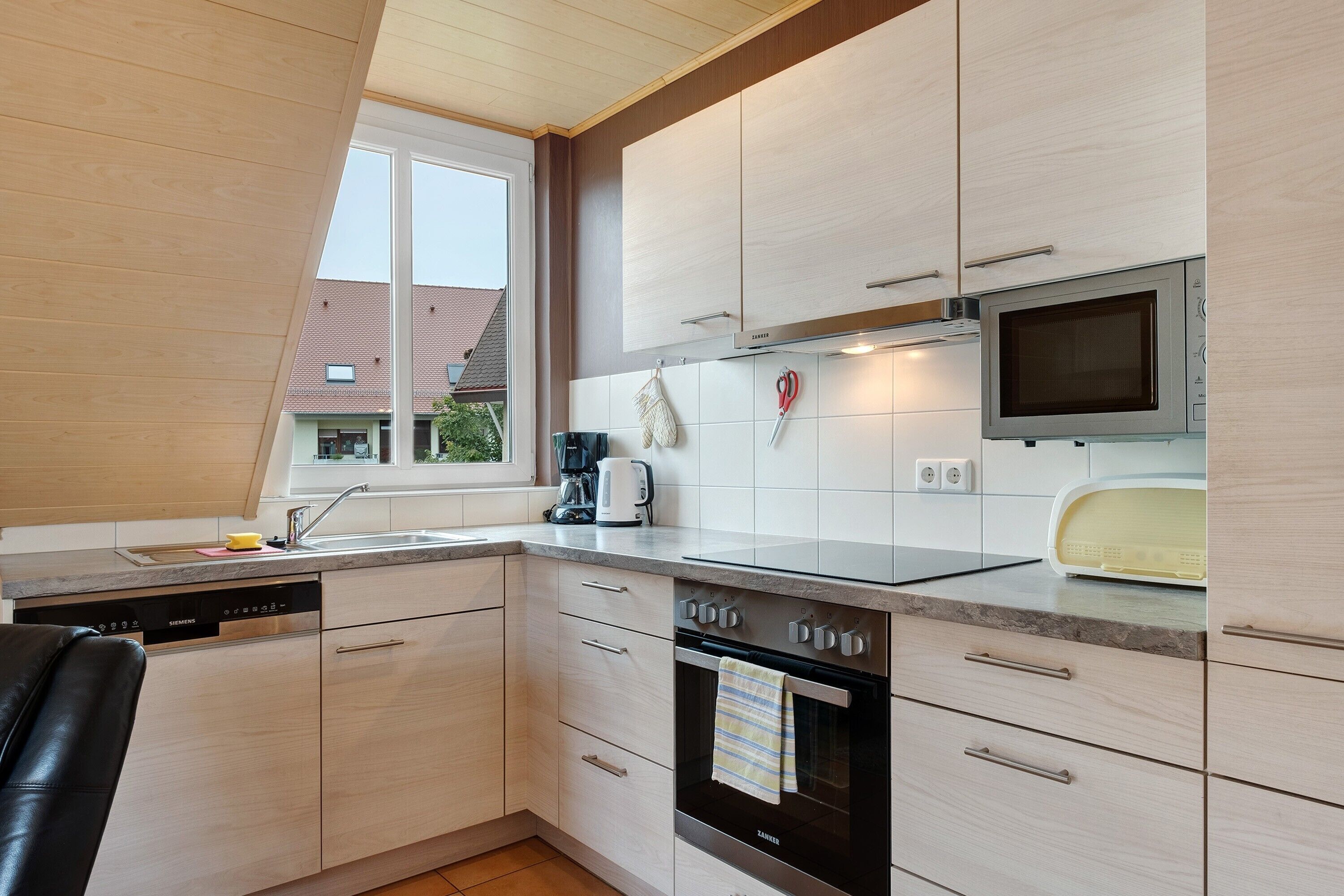 Eine moderne Küche mit Geschirrspüler, Backofen, Mikrowelle und einem Fenster für natürliches Licht.