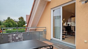 Een balkon met een tafel en stoelen, een schuifdeur die leidt naar een ruimte met een keuken.