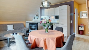 Een moderne woonkamer met een bank, een eettafel met een bloevas en een keuken in de achtergrond.