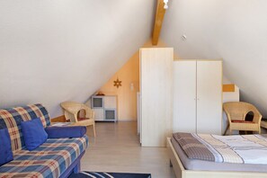 A cozy attic bedroom with a sloped ceiling, a bed, a sofa, and a wardrobe.