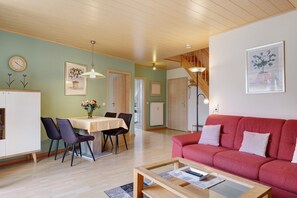 A living room with a red sofa, a dining table with chairs, a kitchen area, and a staircase.