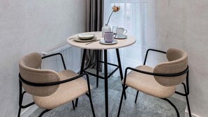 Habitación de esquina con una mesa redonda, dos sillas, un radiador y una ventana con cortinas.