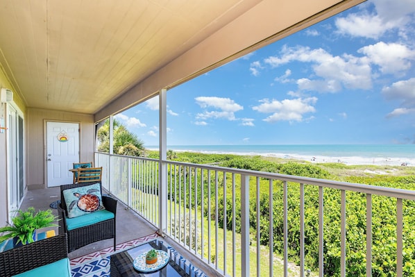 A balcony with wicker furniture, a door, and a view of the beach.