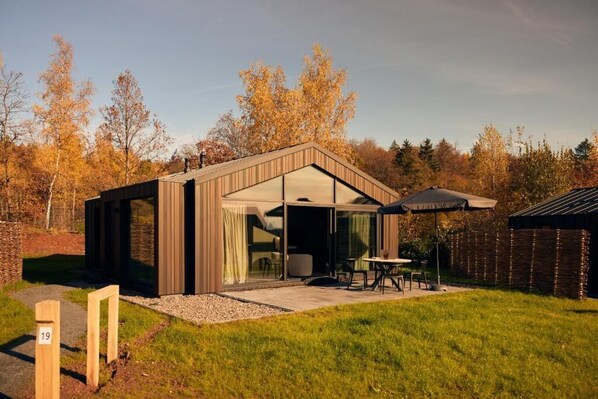 A modern house with a glass door entrance, a patio with outdoor furniture, and a garden. - Harz Eco Lodges (Bad Sachsa)