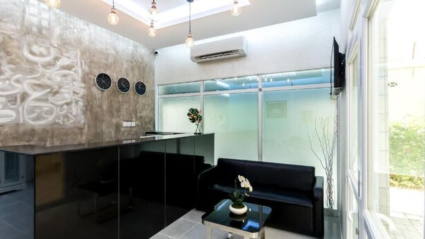 A modern reception area with a glass partition, a black sofa, a glass coffee table with a flower, and a wall with abstract art. - Al Jisr Hotel (Muscat)