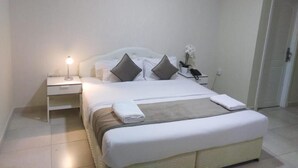 A neatly arranged hotel room with a bed, bedside table, lamp, and a telephone. - Al Jisr Hotel (Muscat)