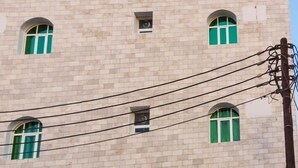 A building with a sign reading "Al Jisr hotel" in Arabic. The building has multiple windows with green curtains. - Al Jisr Hotel (Muscat)