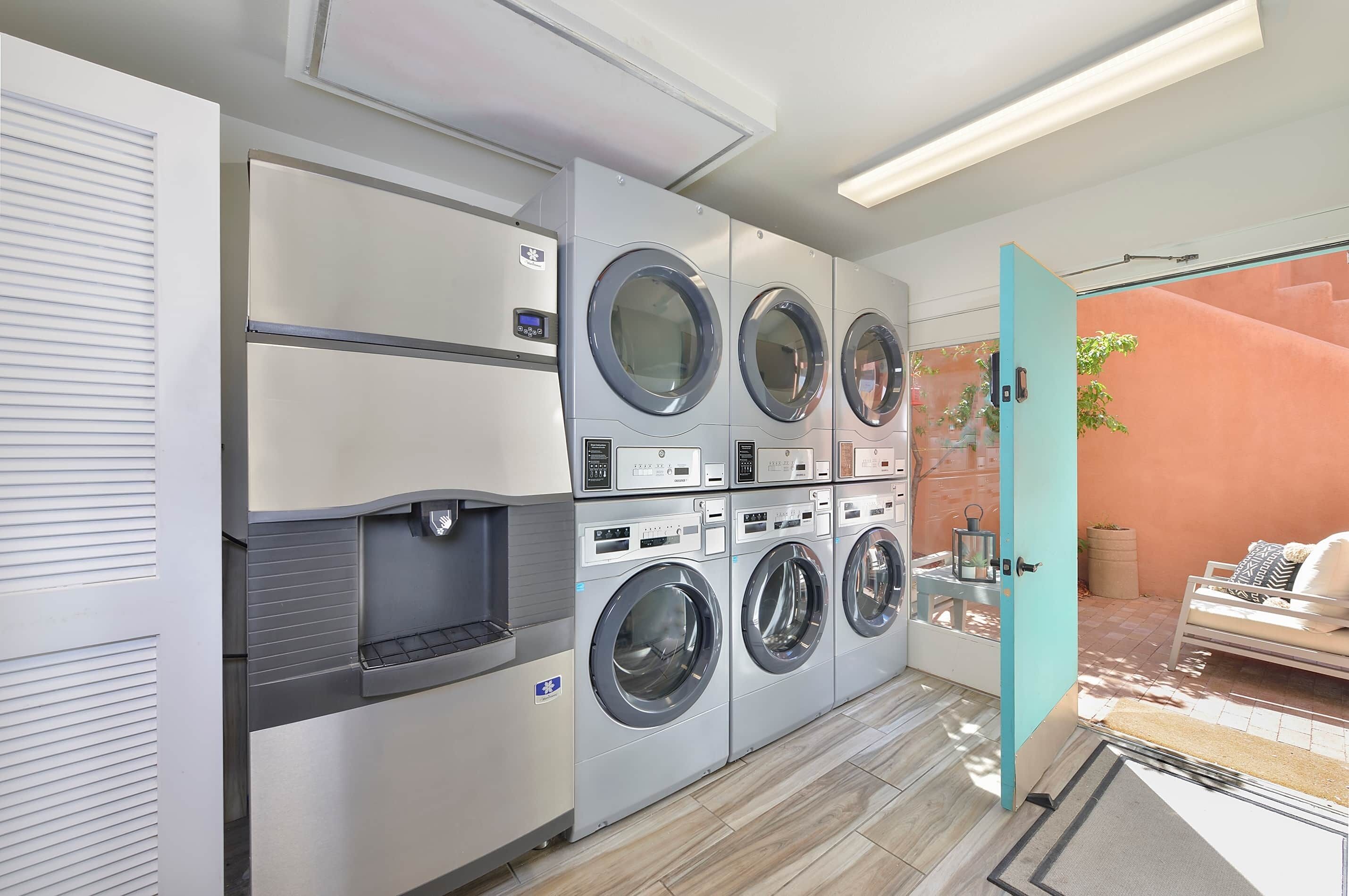 A laundry room with multiple washing machines and dryers, a water dispenser, and a small seating area with a bench and cushions.