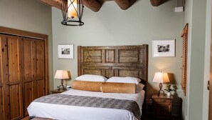 A bedroom with a large bed, wooden headboard, two bedside tables with lamps, and a wooden bench.