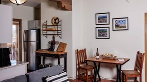 A cozy living area with a sofa, a dining table with chairs, a kitchen with a refrigerator, and a ceiling light fixture.