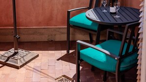 A patio with a table and chairs, a teal umbrella, and a bottle of wine.