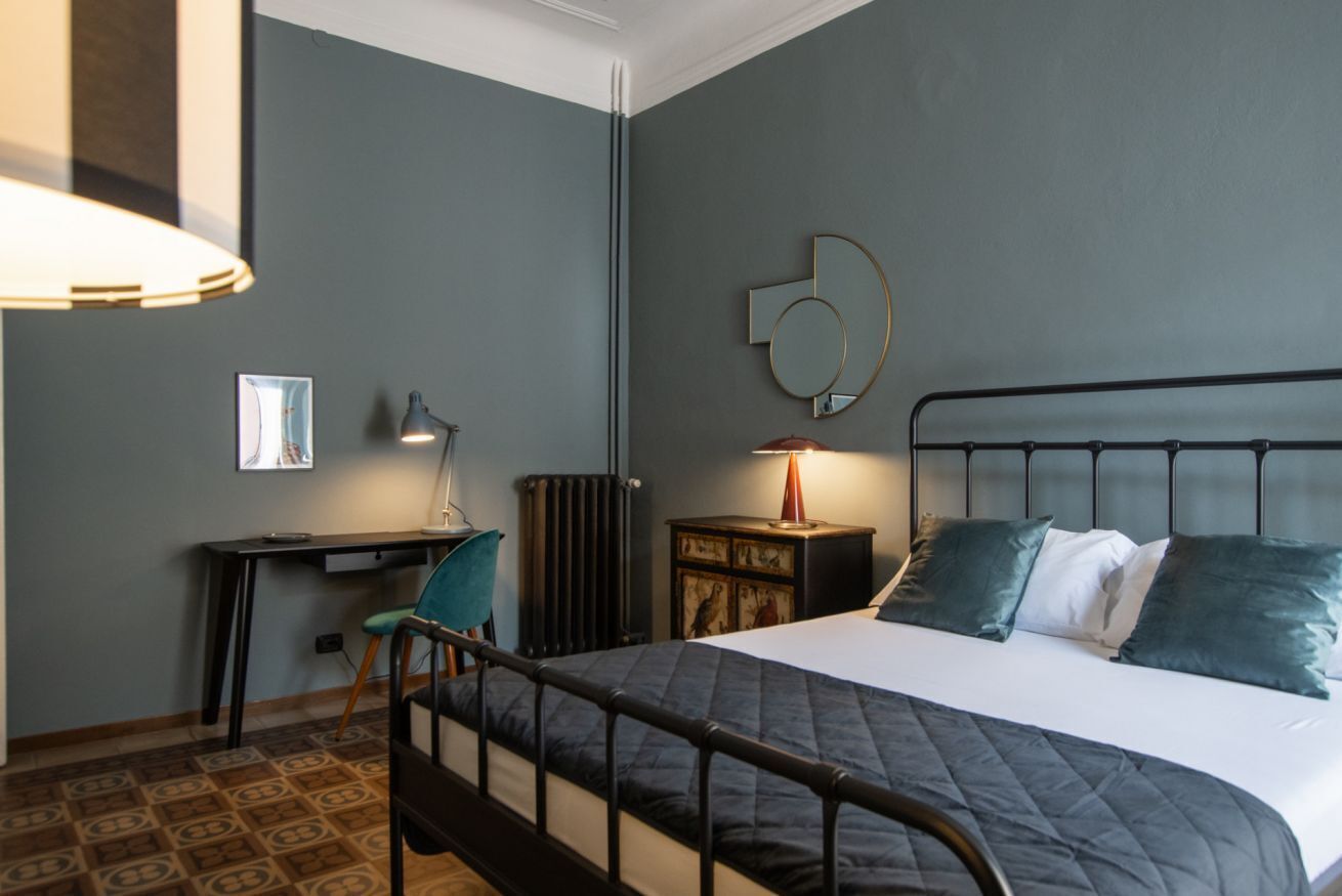 Ein Schlafzimmer mit Bett, Schreibtisch, Stuhl, Heizkörper und einem Wandspiegel.