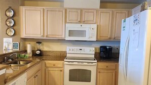 Una cocina con armarios de madera, microondas blanco, estufa y refrigerador.