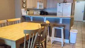 Cocina compacta con una mesa y sillas de madera, microondas, cafetera y refrigerador.
