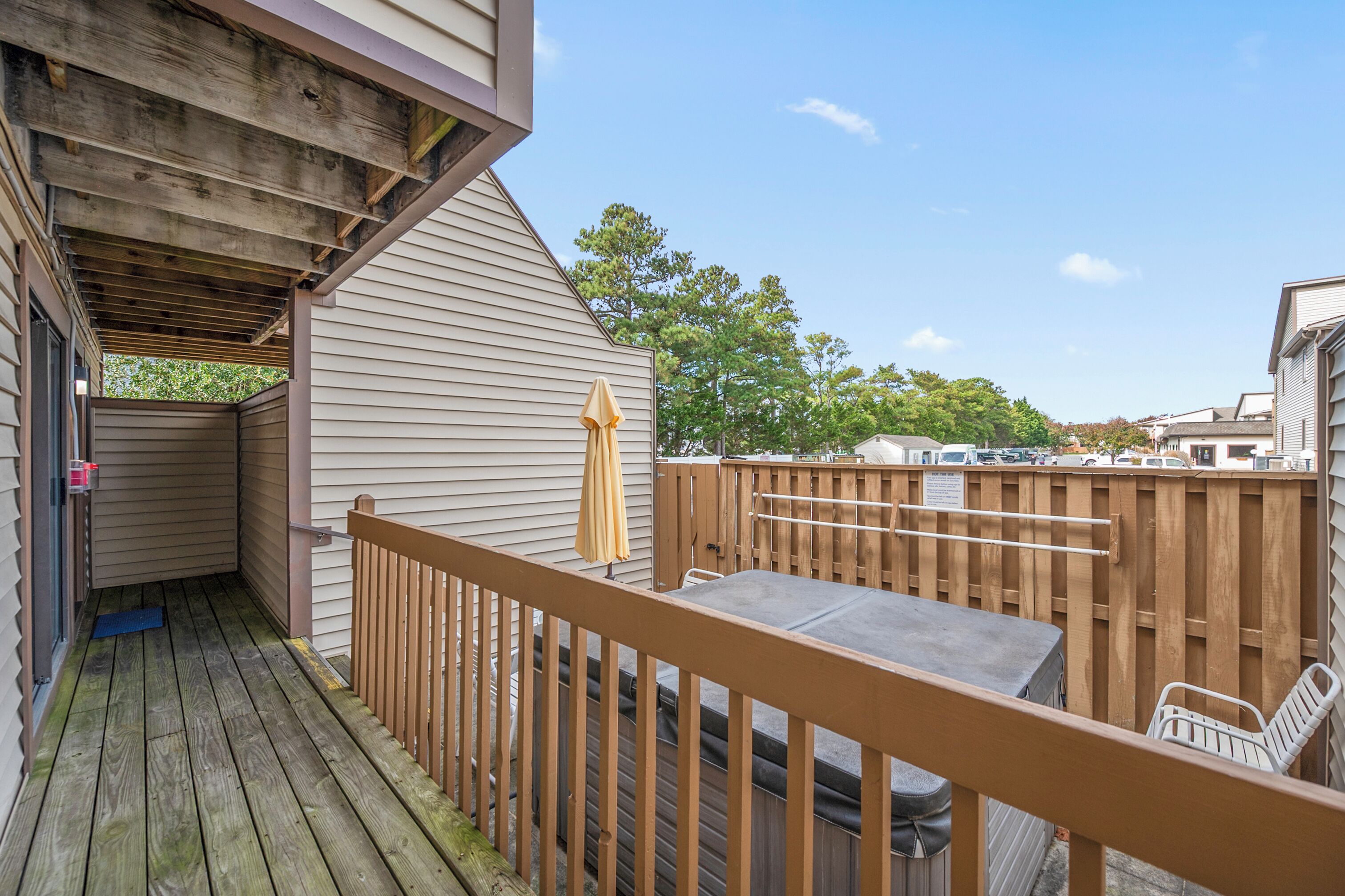 A wooden deck with a table and chairs, a covered area with a bench, and a fenced backyard.