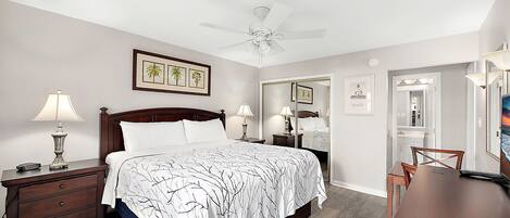A bedroom with a bed, nightstands, a desk, a chair, a ceiling fan, and framed pictures on the wall.