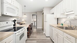 Una cocina moderna con armarios blancos, horno empotrado, microondas, lavaplatos y un comedor con sillas.