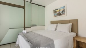 Un dormitorio con cama, mesita de noche, un cuadro en la pared y un ventanal grande.
