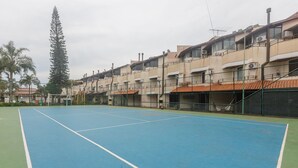 Cancha de tenis con red, rodeada por una valla, y edificios cercanos con balcones.