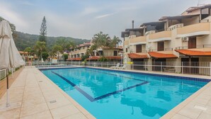 Una piscina con bordes de azulejos, rodeada de edificios con balcones y un paisaje montañoso de fondo.