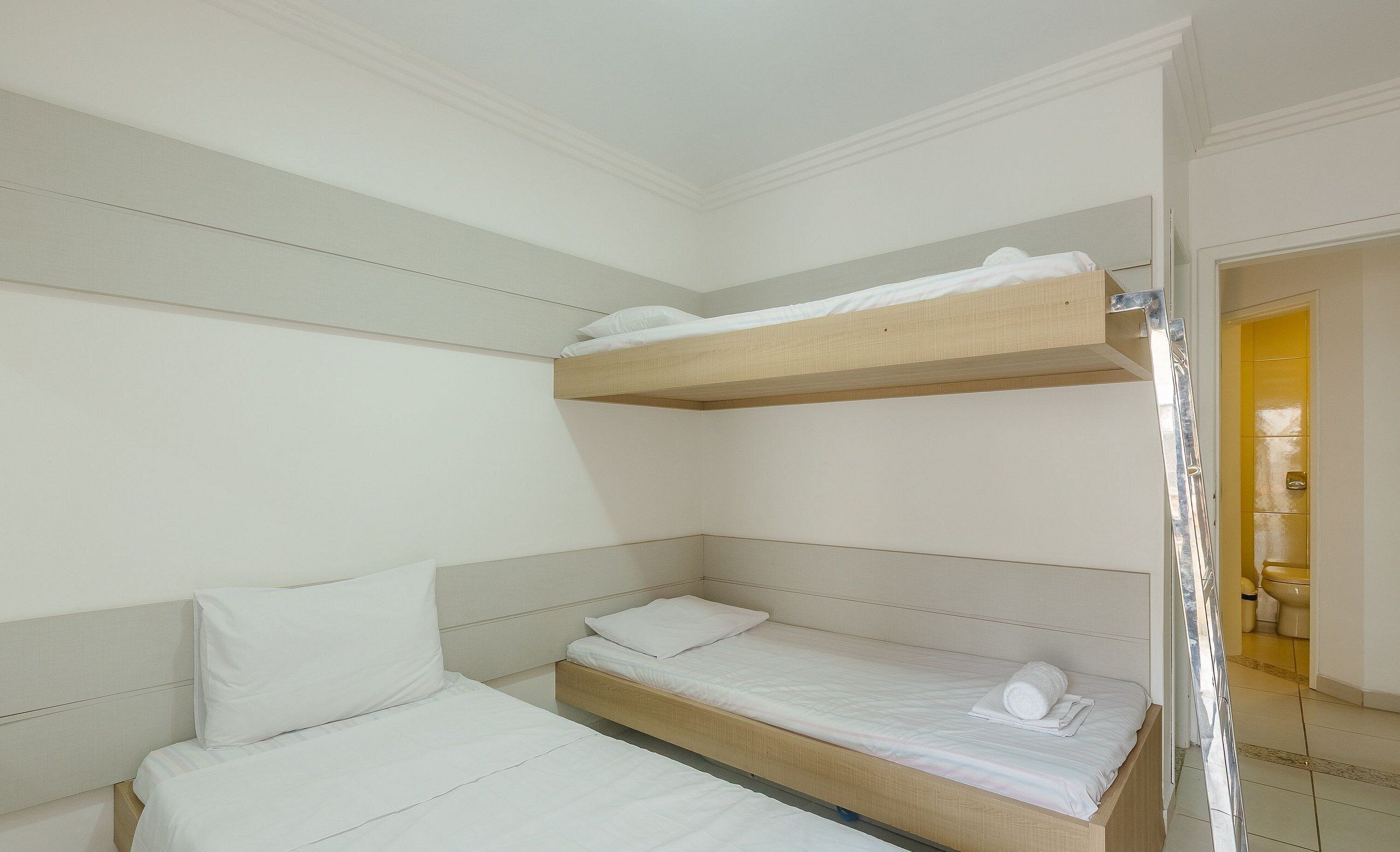 A room with a bunk bed, a single bed, and a bathroom visible through an open door.