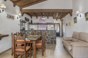 Uma área de jantar com uma ilha de pedra, cadeiras de madeira, uma mesa de vidro e um sofá bege.