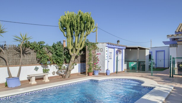 A swimming pool with a tiled edge, surrounded by a fence, a cactus, and a building with a blue door. - Holiday Home 'Isabel' with Private Pool, Wi-Fi and Air Conditioning (Conil de la Frontera)
