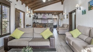 A spacious living area with a high wooden ceiling, two sofas with green cushions, a coffee table, and a kitchen in the background. - Holiday Home 'Isabel' with Private Pool, Wi-Fi and Air Conditioning (Conil de la Frontera)