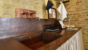 A rustic kitchen with a copper sink, a black wire basket, and a glass display case with pastries.