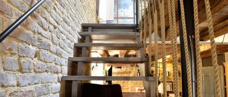 Una escalera estrecha con una pared de ladrillo rústico a un lado y un techo de madera al otro.