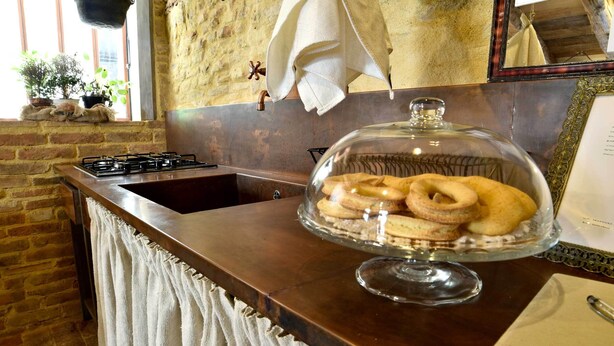 A kitchen with a brick wall, a window with plants, a stove, and a glass display case with cookies.