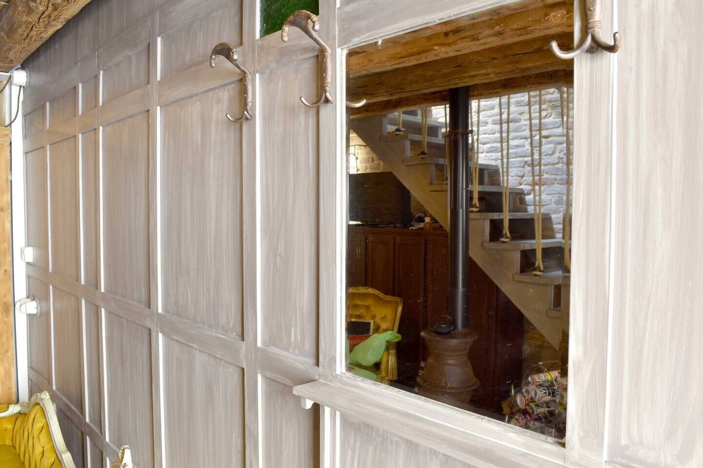 A room with a wooden staircase, a green chair, and a window with a view of a brick wall.