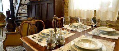 Mesa de comedor dispuesta con platos, vasos y cubiertos, con una radio antigua y una pared de ladrillo al fondo.
