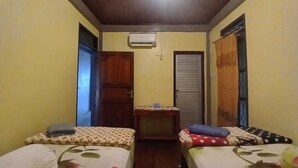 A small, cozy room with two beds, a wooden ceiling, and an air conditioning unit.