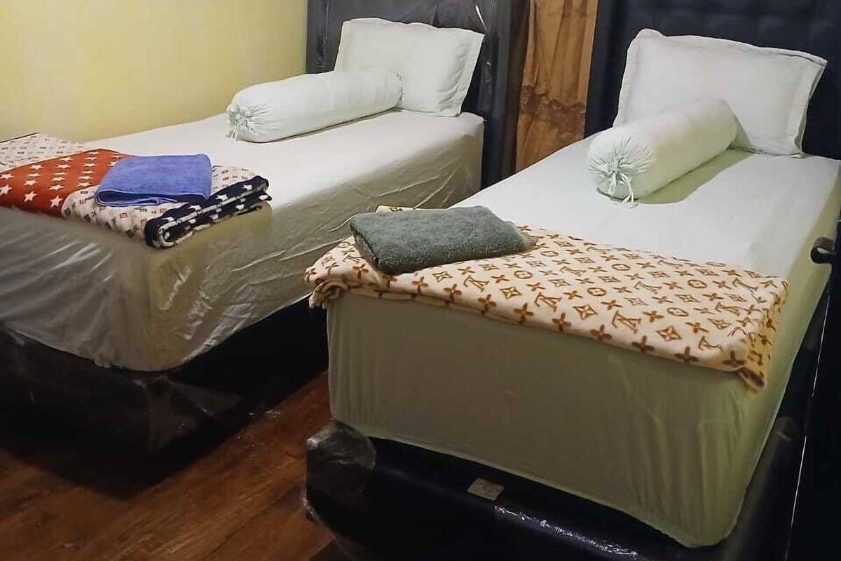 Deux lits simples avec des têtes de lit, une fenêtre avec des rideaux et un plancher en bois.