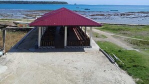 A small building with a red roof, a covered porch, and a dirt path leading to it.