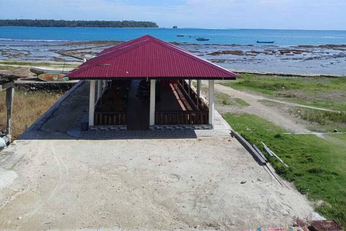 Un petit bâtiment avec un toit rouge, une véranda et un chemin de terre qui y mène.