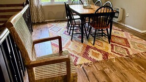 Un coin repas avec une table et des chaises en bois, un tapis à motifs et une fenêtre avec des rideaux.