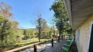 Une terrasse en bois avec des chaises vertes, donnant sur une rivière et des arbres.