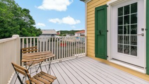 A wooden deck with two chairs, a white fence, and a yellow building with a green door and window. - Queen's Promise - King Suite - AC - Walkable (Christiansted)