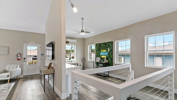 A modern interior with a staircase, a flat-screen TV, a green wall decoration, and a white door marked "EXIT". - Queen's Promise - King Suite - AC - Walkable (Christiansted)
