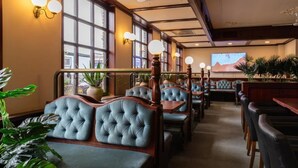 A restaurant with booths and tables, large windows, and wall-mounted lights.