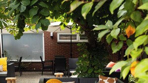 An outdoor seating area with wicker furniture, a potted plant, and a brick wall in the background.