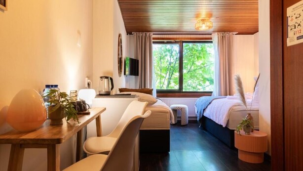 A modern room with a wooden desk, chairs, a bed, and a TV.