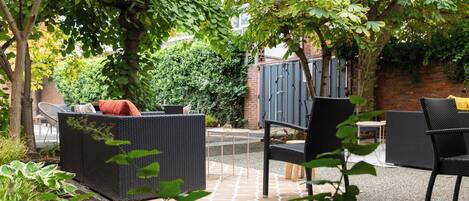 An outdoor patio area with wicker furniture, a brick wall, and greenery.