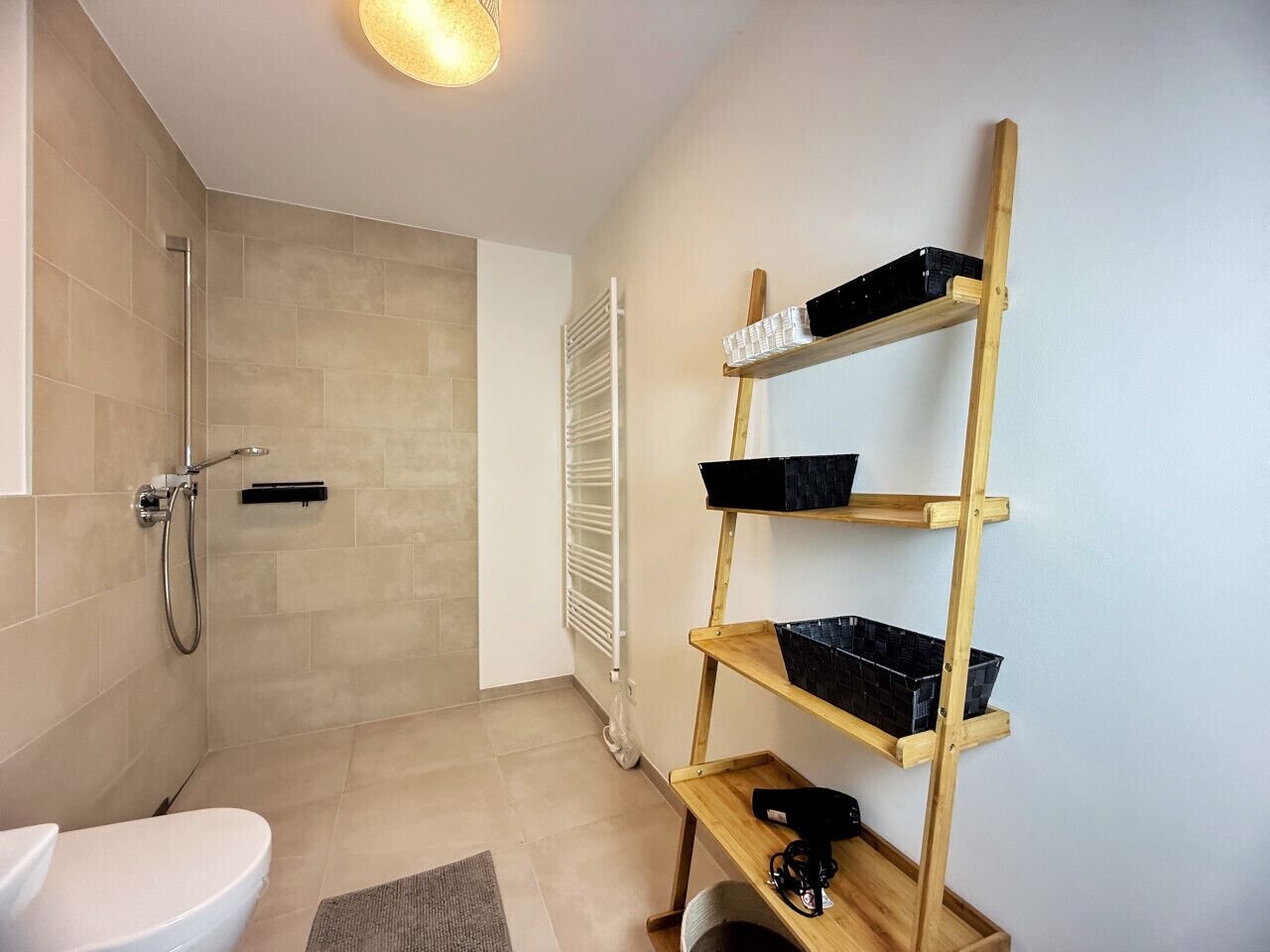 Et moderne badeværelse med bruser, toilet og træhylder med sorte beholdere.